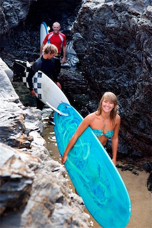 simsearch:649-01696512,k - Three people carrying surfboards by large rocks smiling. Stock Photo - Premium Royalty-Free, Code: 649-01695976