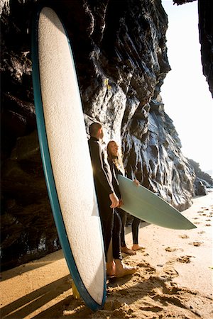 simsearch:649-01696405,k - Couple standing with surfboards by large rocks smiling. Stock Photo - Premium Royalty-Free, Code: 649-01696030