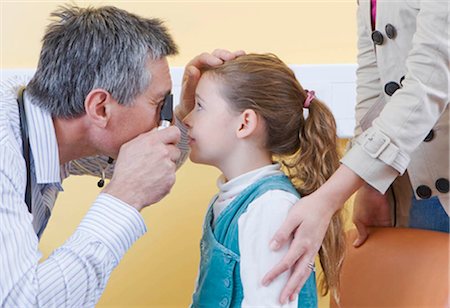 doctor and worried parents - An Optometrist looks into a girls eye Stock Photo - Premium Royalty-Free, Code: 649-02666315