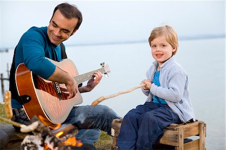 summer camping fire - boy,man with guitar roasting sausages Stock Photo - Premium Royalty-Free, Code: 649-03009378