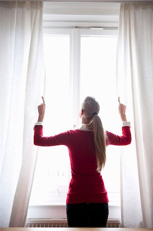 Woman opening window curtains Stock Photo - Premium Royalty-Free, Code: 649-03566100