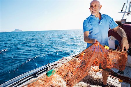 simsearch:400-05676936,k - Fisherman on boat pulling in nets Stock Photo - Premium Royalty-Free, Code: 649-03770754