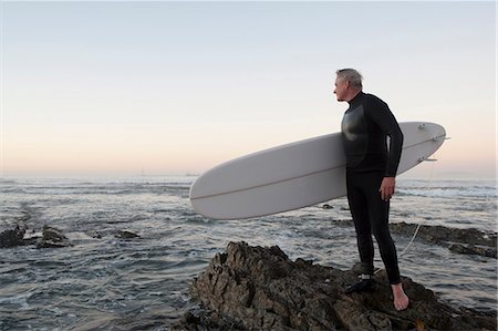 Surfer standing on rocky beach Stock Photo - Premium Royalty-Free, Code: 649-03882126