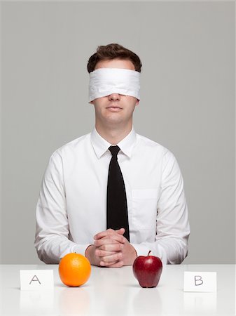 Studio portrait of young man with blindfold choosing between orange and apple Stock Photo - Premium Royalty-Free, Code: 640-05761250