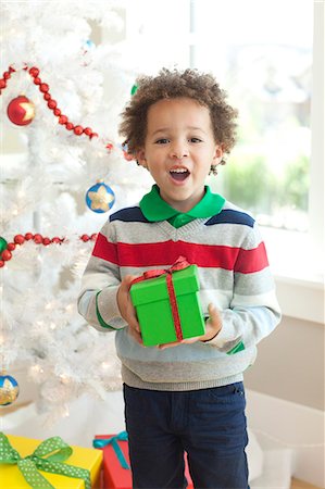 Young boy sitting under Christmas tree, holding Christmas present Stock Photo - Premium Royalty-Free, Code: 640-06963469