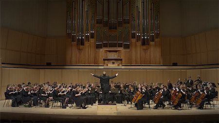 Rear view of conductor gesturing and leading music orchestra in auditorium Stock Photo - Premium Royalty-Free, Code: 640-09013304