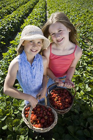 Portrait of two girls with baskets of strawberries on a field Stock Photo - Premium Royalty-Free, Code: 640-01348598