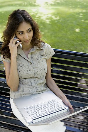 simsearch:640-02767760,k - Vue grand angle d'une jeune femme tenant un ordinateur portable parler sur un téléphone mobile Photographie de stock - Premium Libres de Droits, Code: 640-01349151