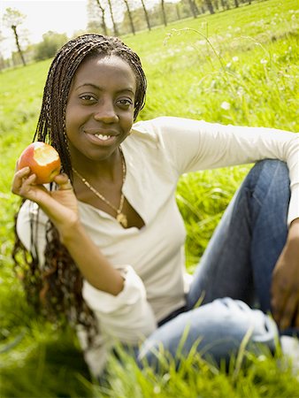 Portrait of a teenage girl sitting in a field and holding an apple Stock Photo - Premium Royalty-Free, Code: 640-01349399