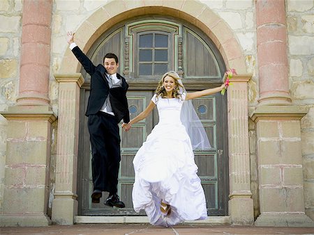 Bride and groom jumping and holding hands outside with bouquet Stock Photo - Premium Royalty-Free, Code: 640-01354266