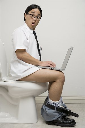 Portrait of a young man sitting on a toilet using a laptop Stock Photo - Premium Royalty-Free, Code: 640-01357348