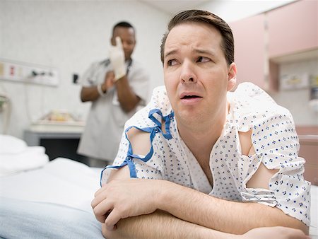 A nervous patient lying on the bed with a doctor putting on latex gloves in the background Stock Photo - Premium Royalty-Free, Code: 640-01357752