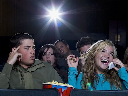 Girl talking on cell phone at movie theater with annoyed boy Stock Photo - Premium Royalty-Free, Code: 640-01357890