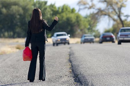 Woman hitchhiking while holding a gas can Stock Photo - Premium Royalty-Free, Code: 640-01358565