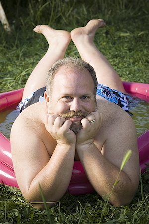 fat man at swimming pool - Overweight man in inflatable wading pool Stock Photo - Premium Royalty-Free, Code: 640-01358607