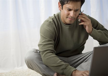 shag carpet - Close-up of a man talking on a mobile phone and looking at his laptop Stock Photo - Premium Royalty-Free, Code: 640-01359036