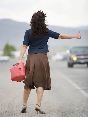 Rear view of a young woman holding a gas can and hitchhiking Stock Photo - Premium Royalty-Free, Code: 640-01359231