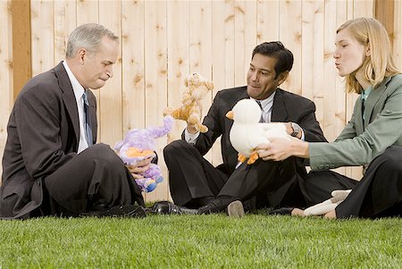 Two businessmen and a businesswoman playing with toys sitting on a lawn Stock Photo - Premium Royalty-Free, Code: 640-01350618