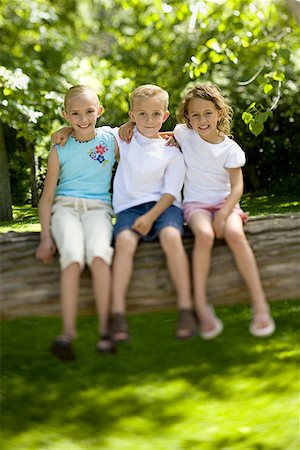 Portrait of two girls and a boy sitting on a tree trunk Stock Photo - Premium Royalty-Free, Code: 640-01350866
