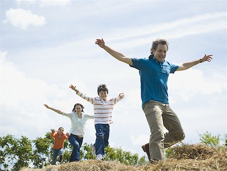 simsearch:640-02767192,k - Low angle view of a man and a woman jumping with their children on hay bales Foto de stock - Sin royalties Premium, Código: 640-01351165