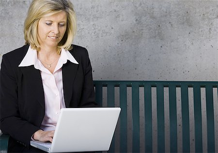 Businesswoman sitting on a bench and using a laptop Stock Photo - Premium Royalty-Free, Code: 640-01364336