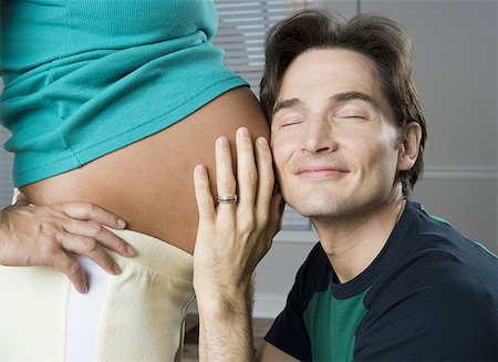 Close-up of a man putting his ear up to a pregnant woman's stomach Stock Photo - Premium Royalty-Free, Code: 640-01364378