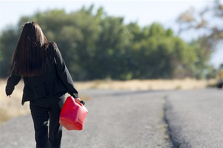 Rear view of a young woman walking and holding a gas can Stock Photo - Premium Royalty-Free, Code: 640-01364871