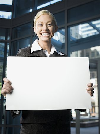 Portrait of a businesswoman holding a blank sign and smiling Stock Photo - Premium Royalty-Free, Code: 640-01365598