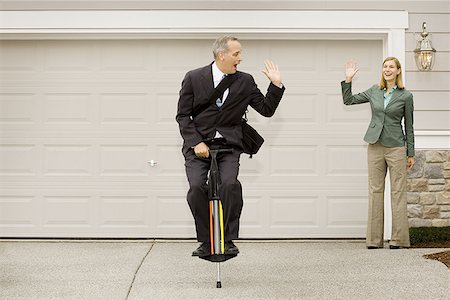 Businessman on a pogo stick waving at a businesswoman Stock Photo - Premium Royalty-Free, Code: 640-01360047