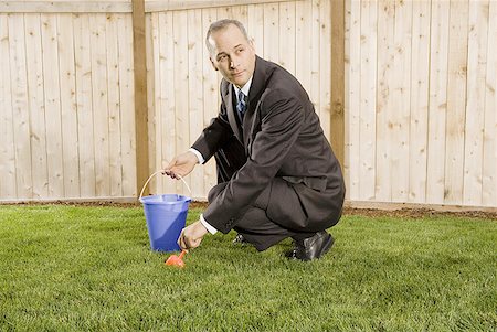 Profile of a businessman crouching on a lawn holding sand pail and shovel Stock Photo - Premium Royalty-Free, Code: 640-01360667