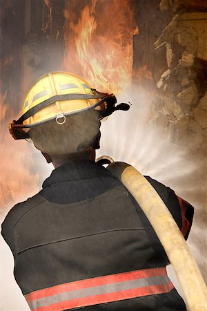 Rear view of a firefighter carrying a fire hose on his shoulder Stock Photo - Premium Royalty-Free, Code: 640-01361891