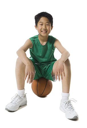 Portrait of a boy sitting on a basketball and smiling Stock Photo - Premium Royalty-Free, Code: 640-01361951