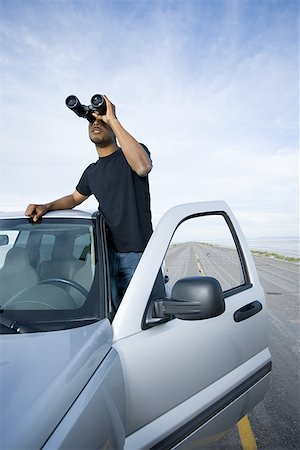 Young man looking through a pair of binoculars Stock Photo - Premium Royalty-Free, Code: 640-01362670