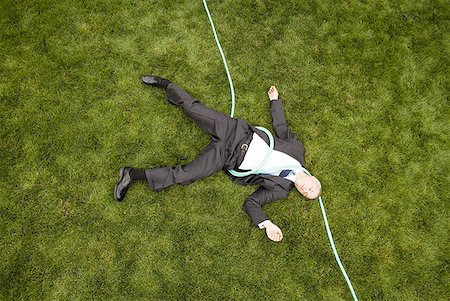High angle view of a businessman with a hose lying down on a lawn Stock Photo - Premium Royalty-Free, Code: 640-01363613