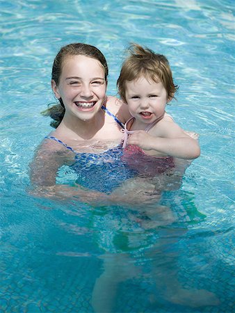 Girl with braces in pool holding younger girl smiling Stock Photo - Premium Royalty-Free, Code: 640-01458830