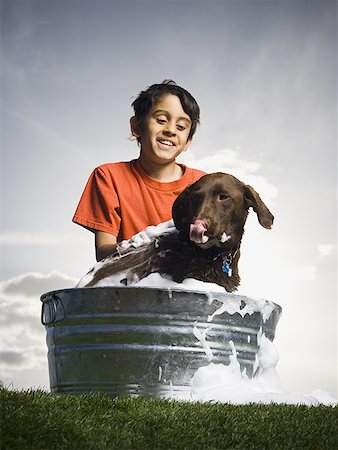 Boy bathing dog outdoors on cloudy day smiling Stock Photo - Premium Royalty-Free, Code: 640-01574896