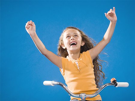 Girl riding bicycle with no hands smiling Stock Photo - Premium Royalty-Free, Code: 640-01574944