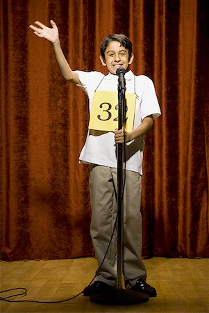 Boy contestant standing at microphone waving and smiling Stock Photo - Premium Royalty-Free, Code: 640-01574993