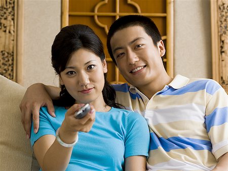 Couple embracing on sofa while woman changes channels with television remote Stock Photo - Premium Royalty-Free, Code: 640-01601440