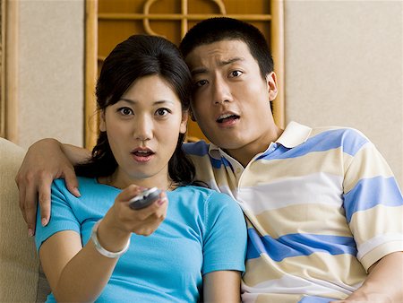 Couple watching television looking shocked with woman holding remote Stock Photo - Premium Royalty-Free, Code: 640-01601441