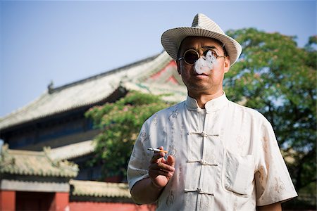 smokers - Man with sunglasses and straw hat smoking cigarette outdoors with pagoda in background Stock Photo - Premium Royalty-Free, Code: 640-02765409