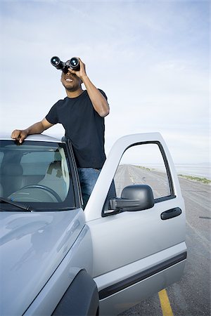 Young man looking through a pair of binoculars Stock Photo - Premium Royalty-Free, Code: 640-02766722