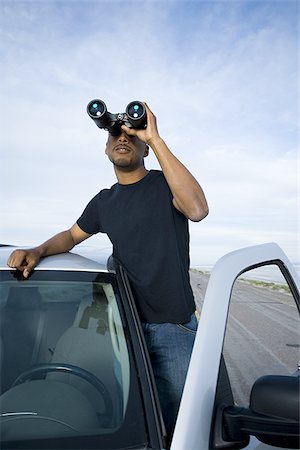 Young man looking through a pair of binoculars Stock Photo - Premium Royalty-Free, Code: 640-02766723
