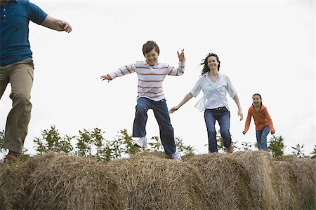 simsearch:640-02767192,k - Low angle view of a man and a woman jumping with their children on hay bales Foto de stock - Sin royalties Premium, Código: 640-02767584