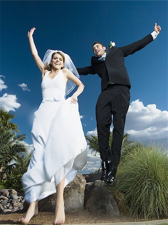 Low angle view of a newlywed couple holding hands and jumping Stock Photo - Premium Royalty-Free, Code: 640-02768129