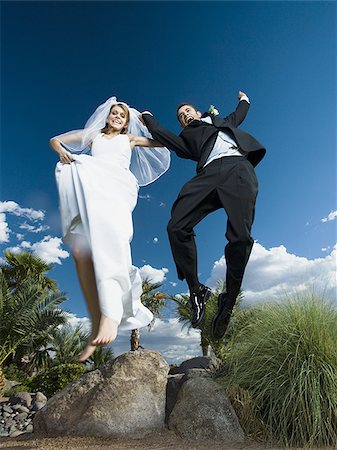 Low angle view of a newlywed couple holding hands and jumping Stock Photo - Premium Royalty-Free, Code: 640-02768130