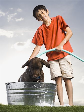 Boy bathing dog outdoors on cloudy day smiling Stock Photo - Premium Royalty-Free, Code: 640-02774338