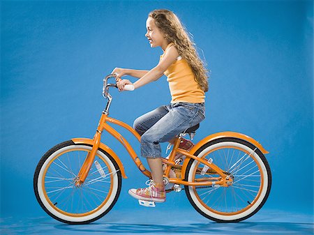 Girl riding orange bicycle profile Stock Photo - Premium Royalty-Free, Code: 640-02774418