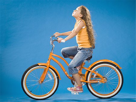 Girl riding orange bicycle profile Stock Photo - Premium Royalty-Free, Code: 640-02774419