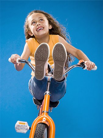 riding on bicycles handle bars - Girl riding orange bicycle with feet on handlebars smiling Stock Photo - Premium Royalty-Free, Code: 640-02774427